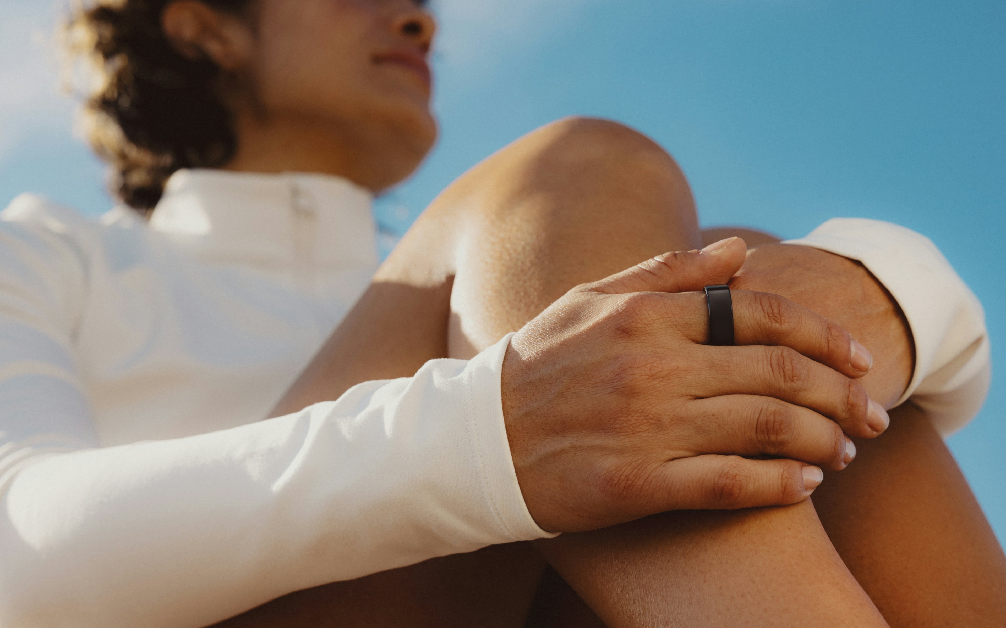 一名佩戴著 Oura Ring 的女人,將手放在膝上,圖片上疊加應用程式外觀的圖樣