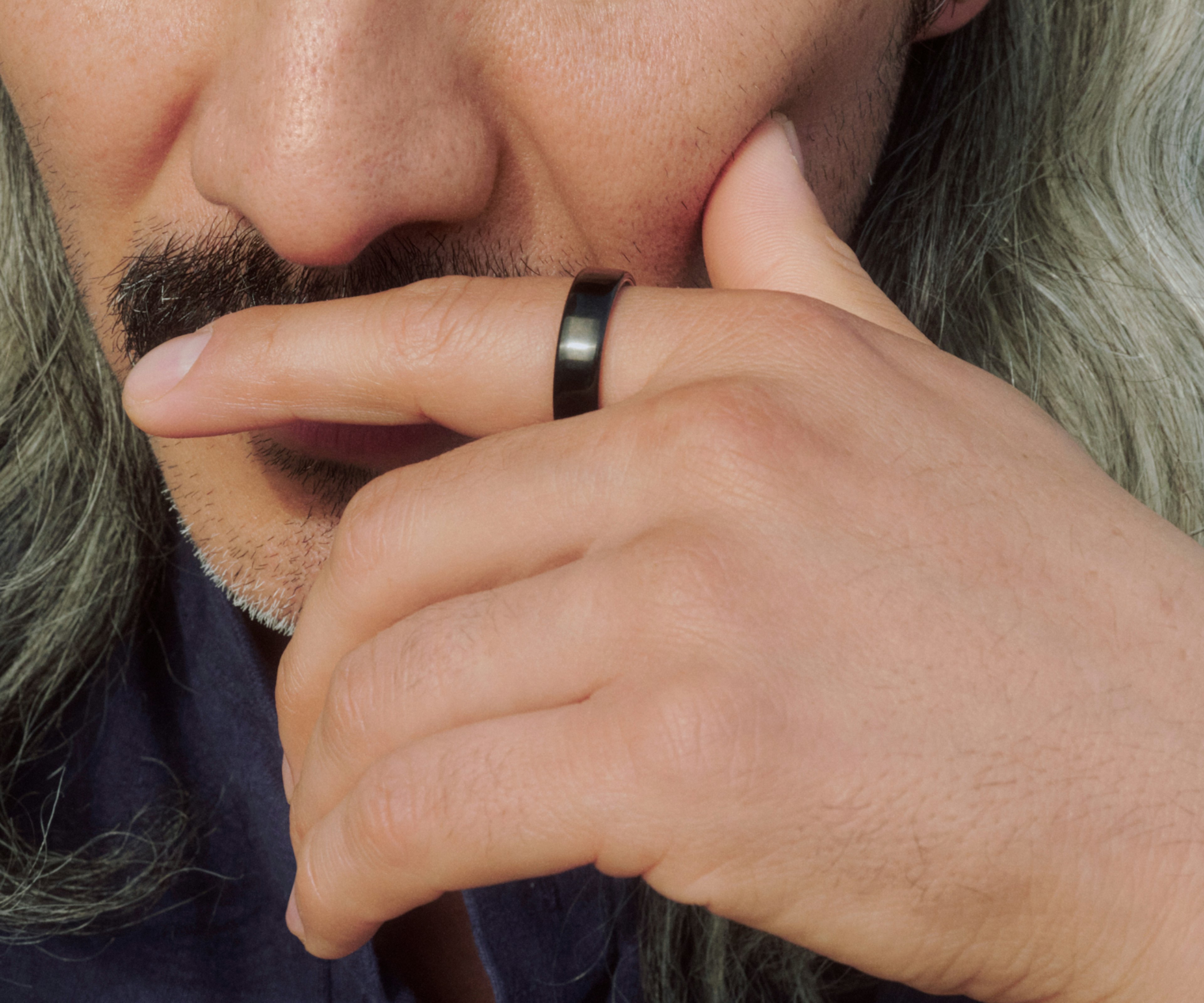 特写镜头：一名男子佩戴 Black Oura Ring 5，指尖轻抵唇边，神态若有所思。