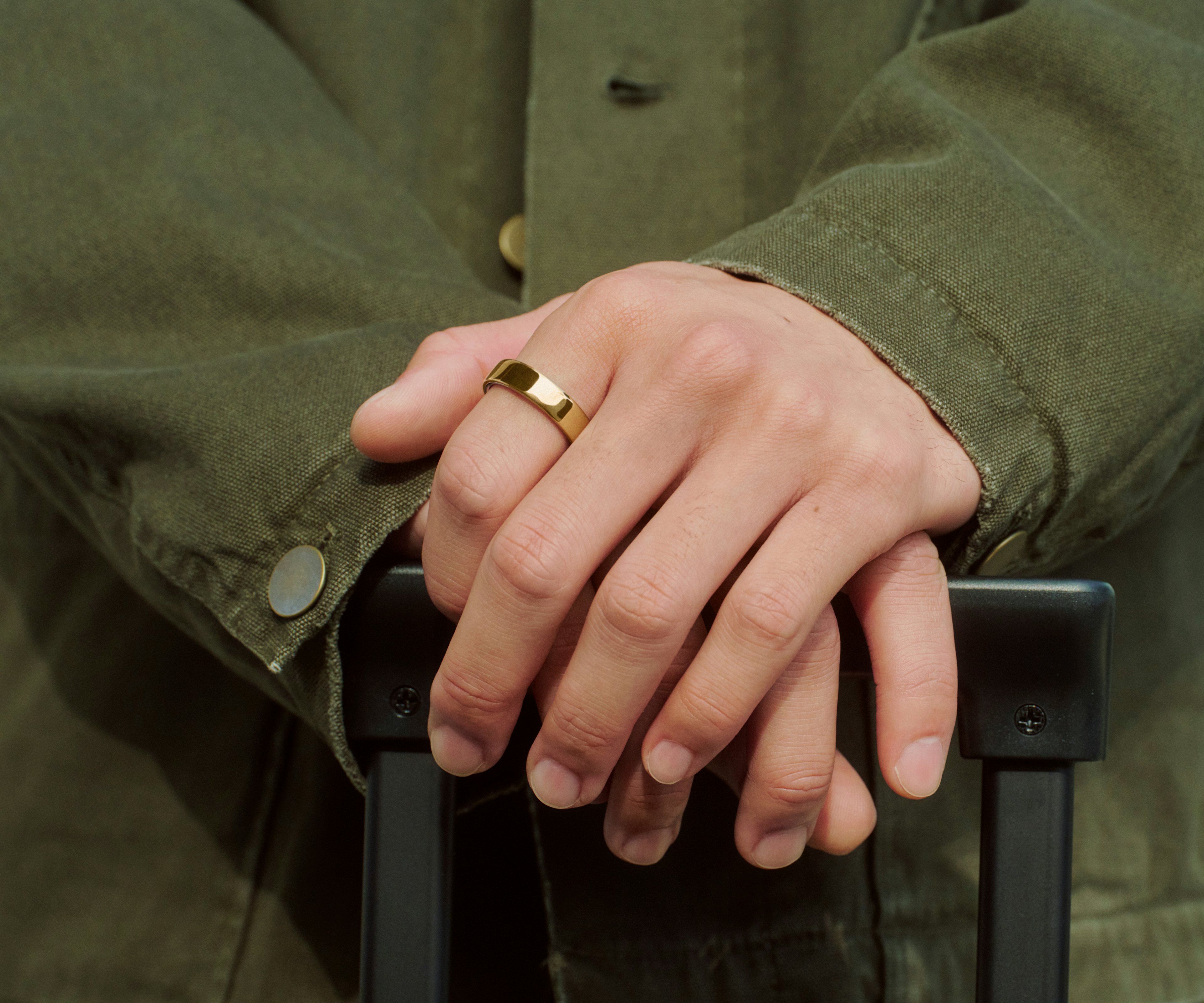 特写：一个人双手搭在旅行箱拉杆上，手指上佩戴着 Gold 饰面的 Oura Ring 5