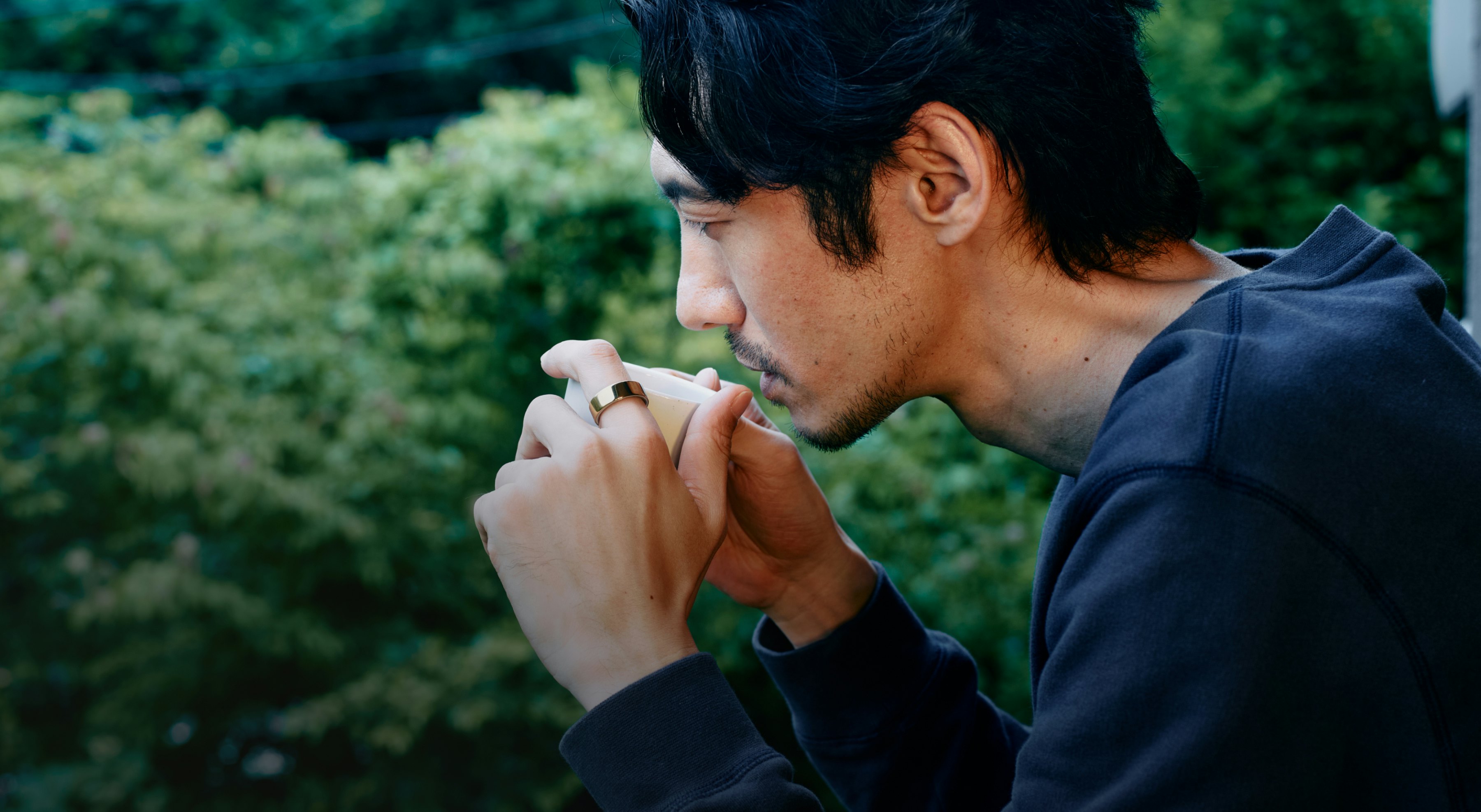 カップから飲み物を飲もうとしているOura Ringを指に着用した男性。
