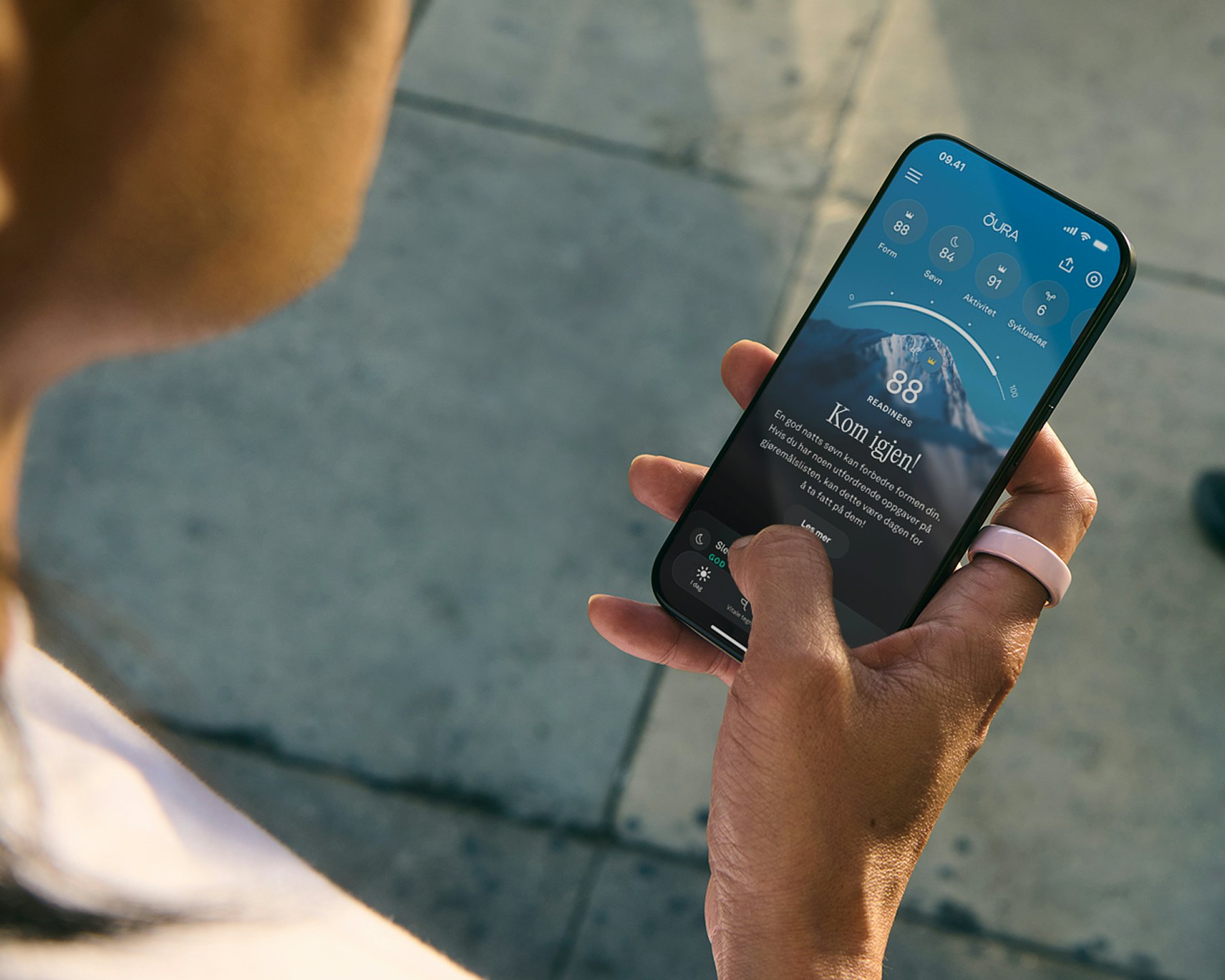 En person ser på Oura-appen på smarttelefonen sin og har på seg en Petal Oura Ring Ceramic på høyre pekefinger