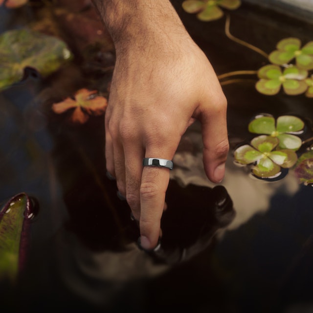 一個人伸手觸碰景觀池的水面，手指上戴著 Silver 色 Oura Ring 5 的特寫