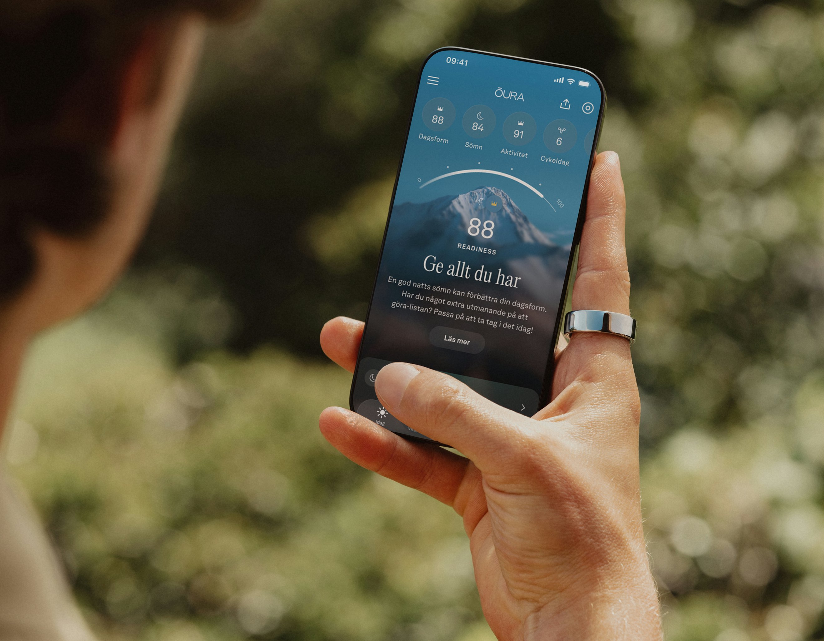 En person som tittar i Oura-appen på sin smarttelefon och bär en Oura Ring på höger pekfinger
