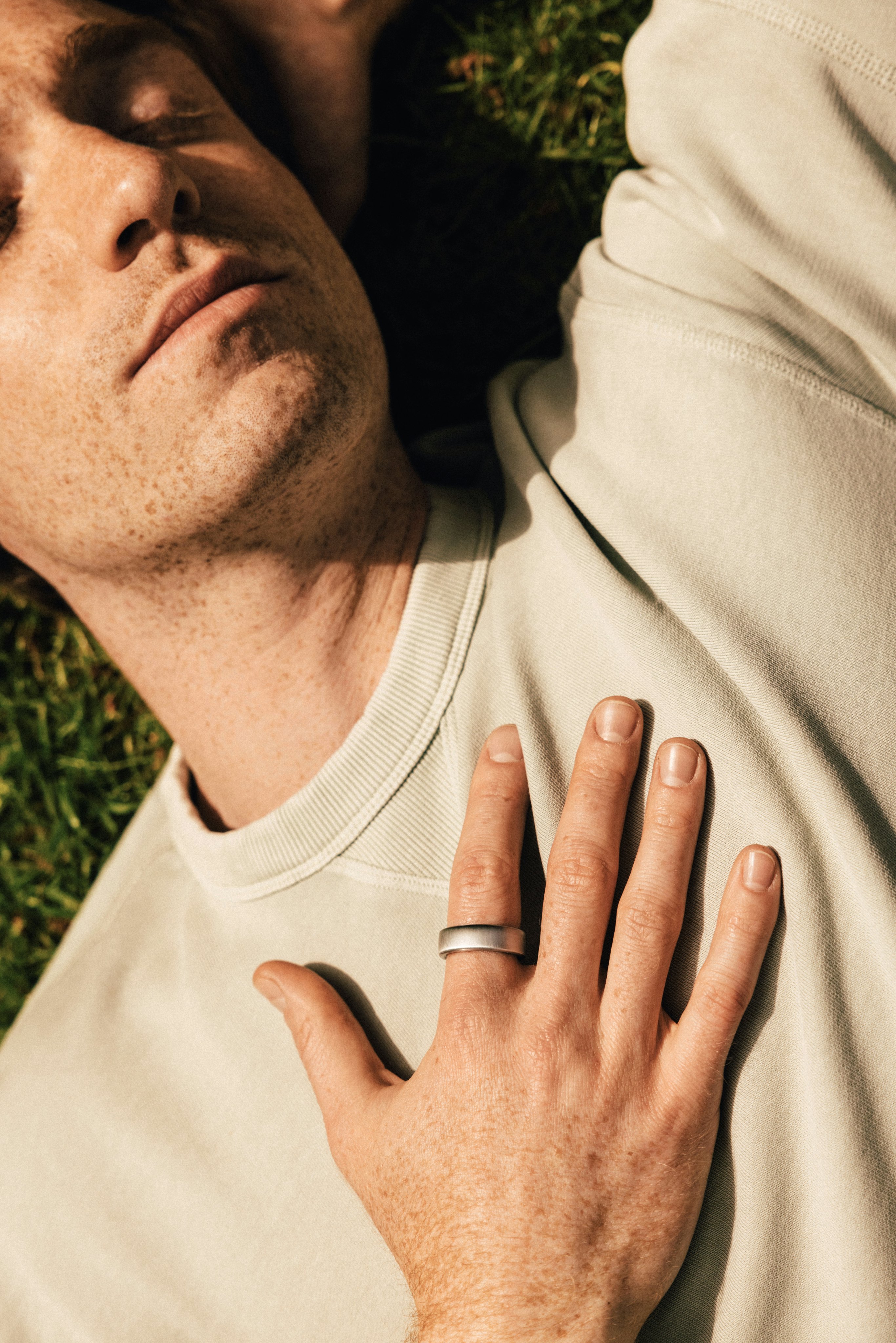 一名男子躺在草地上,右手放在胸前,食指戴著一枚 Oura Ring。